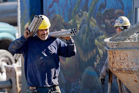 construction worker carrying pipes on his shoulders